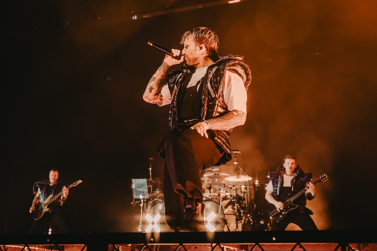Electric Callboy vocalist Nico Sallach singing on stage with bandmates under dramatic orange spotlights.